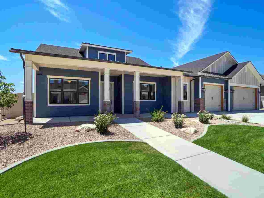 modern landscaped new construction by home construction companies with blue sky and puffy white clouds. Covered front porch with three car garage