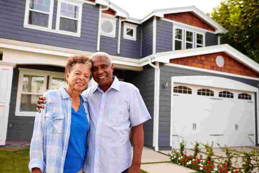 Senior black couple standing outside a large suburban house made by home construction companies.